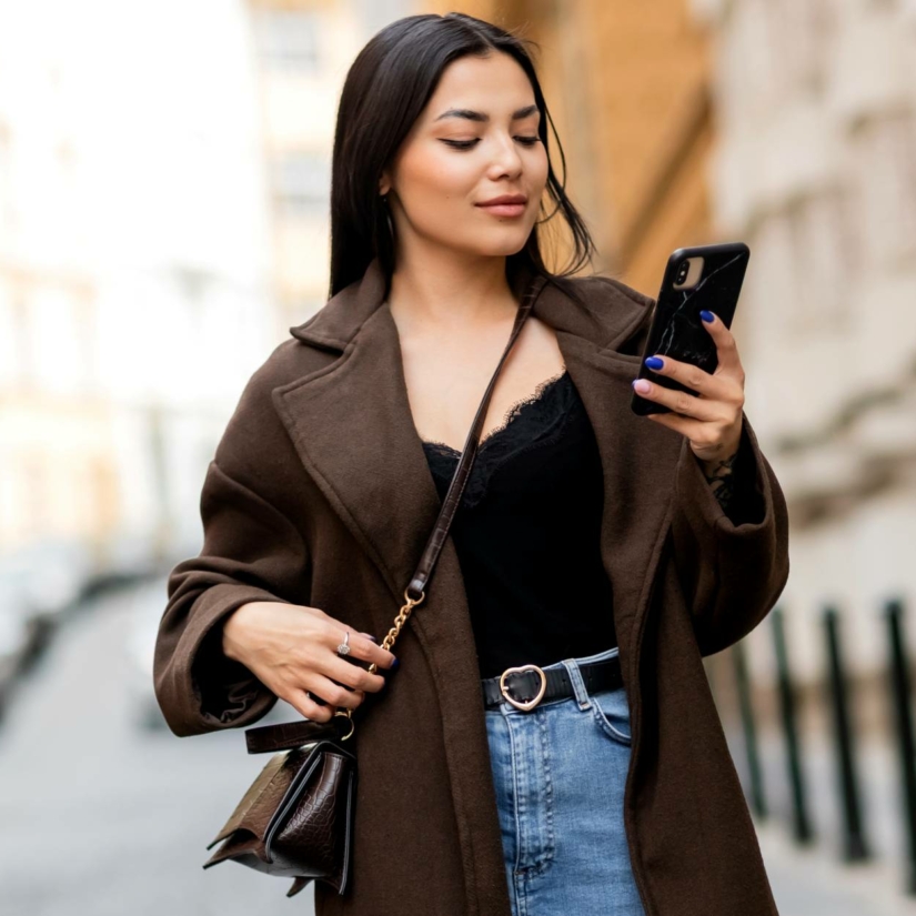 Jeune femme en manteau élégant et jeans tenant des lunettes de soleil © KotykOlenaBO/Depositphotos