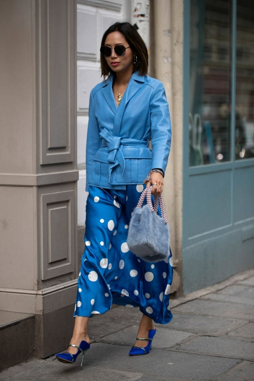 Street style de Fashion Week – Femme avec un vêtement satiné à pois blancs sur fond bleu et une veste à texture cuir bleu vif