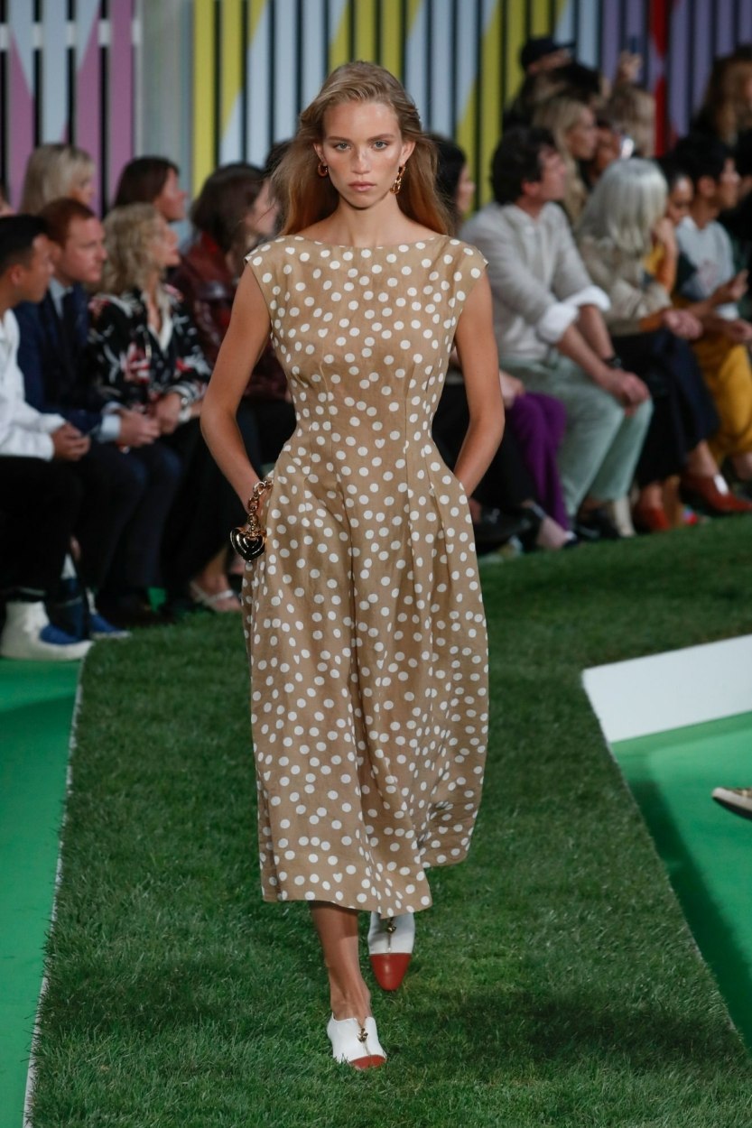 Défilé Escada – Mannequin avec une robe à pois blancs sur fond marron pâle ou beige de longueur midi