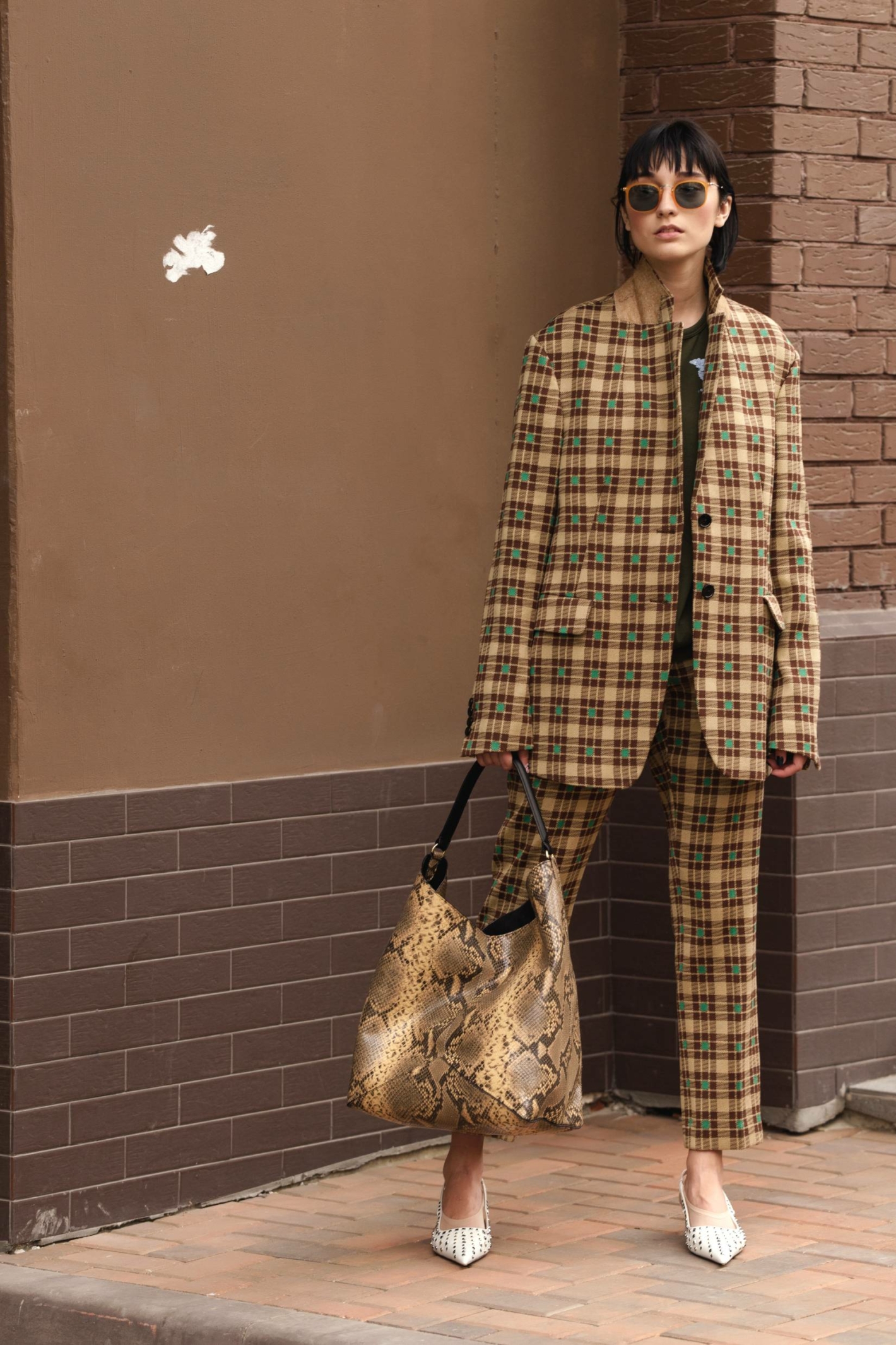 Girl in a beige jacket and trousers on a beige brick background © Street style photo/Shuttertsock