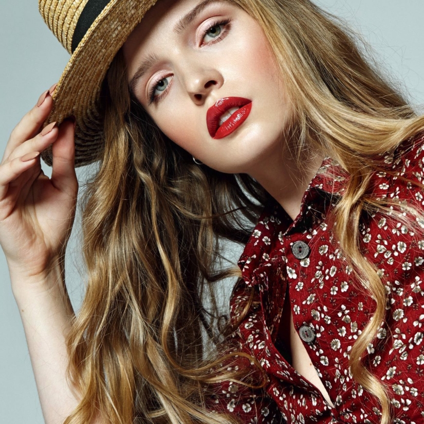 Belle jeune fille romantique aux longs cheveux blonds dans un chapeau de paille et une robe rouge avec de petites fleurs blanches, pensivement dans le cadre © Ekaterina Jurkova/Depositphotos