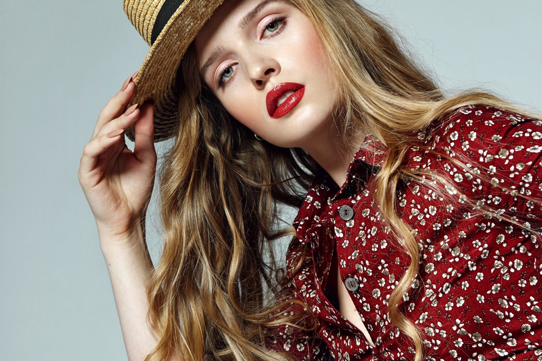 Belle jeune fille romantique aux longs cheveux blonds dans un chapeau de paille et une robe rouge avec de petites fleurs blanches, pensivement dans le cadre © Ekaterina Jurkova/Depositphotos